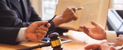 Attorney reviewing text with client.  Gavel in the foreground, book and hands in the background