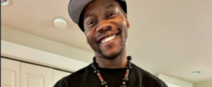 Smiling man with medium dark skin wearing a ball cap.